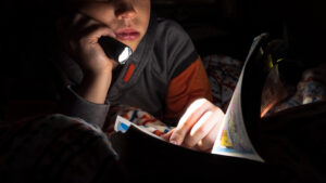 Lapsi lukemassa sarjakuvia pimeässä taskulampun valossa.
